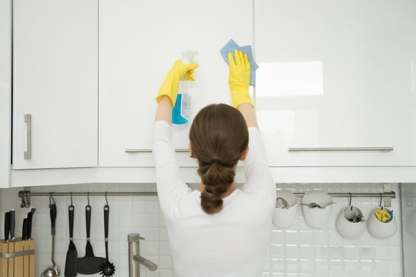 a woman wearing yellow gloves cleaning white cabinets with a spray bottle